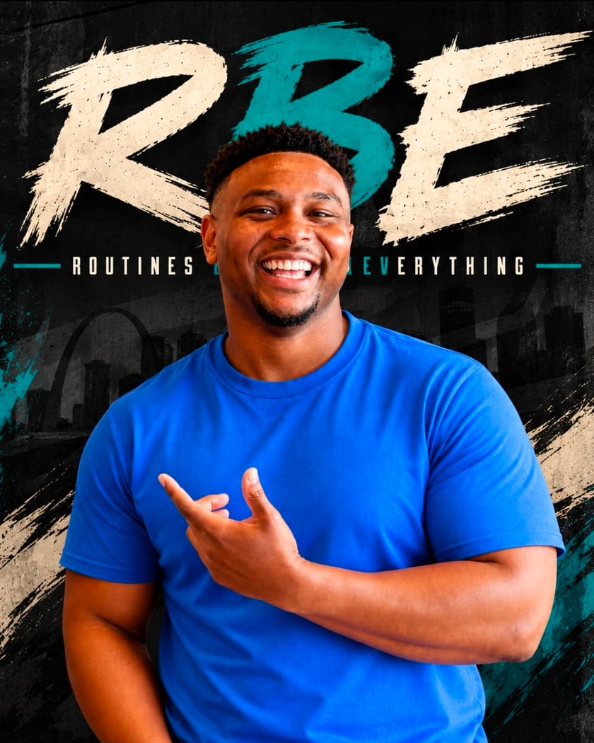 Coach Nick Lunceford, founder of RBE Fitness, smiling in a blue T-shirt in front of an RBE, Routines Build Everything, backdrop.